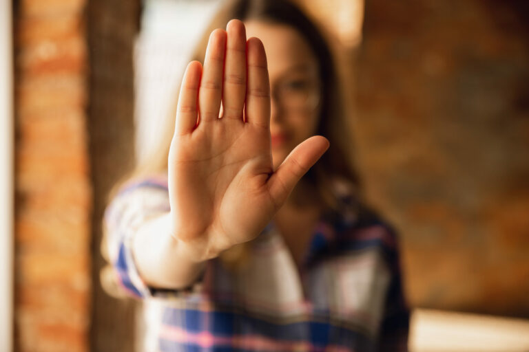 Nahaufnahme einer jungen Frau die eine STOP-Geste mit ihrer Hand macht und damit klare Grenzen aufzeigt
