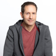 Andreas Schumann, Inhaber des APS-Instituts sitzend und lächelnd mit T-Shirt und grauer Sweatjacke wie zum Beispiel in einem Gewaltpräventionskurs an einer Schule