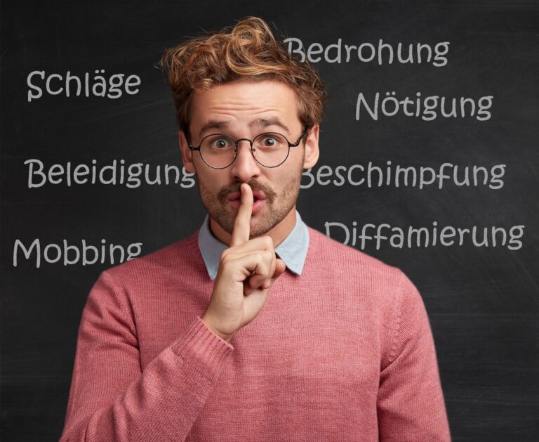 Lehrer vor einer Schultafel mit Begriffen zu verbaler und körperlicher Gewalt hält den Finger vor die Lippen, um zu zeigen, dass das Thema Gewalt gegen Lehrer häufig totgeschwiegen wird